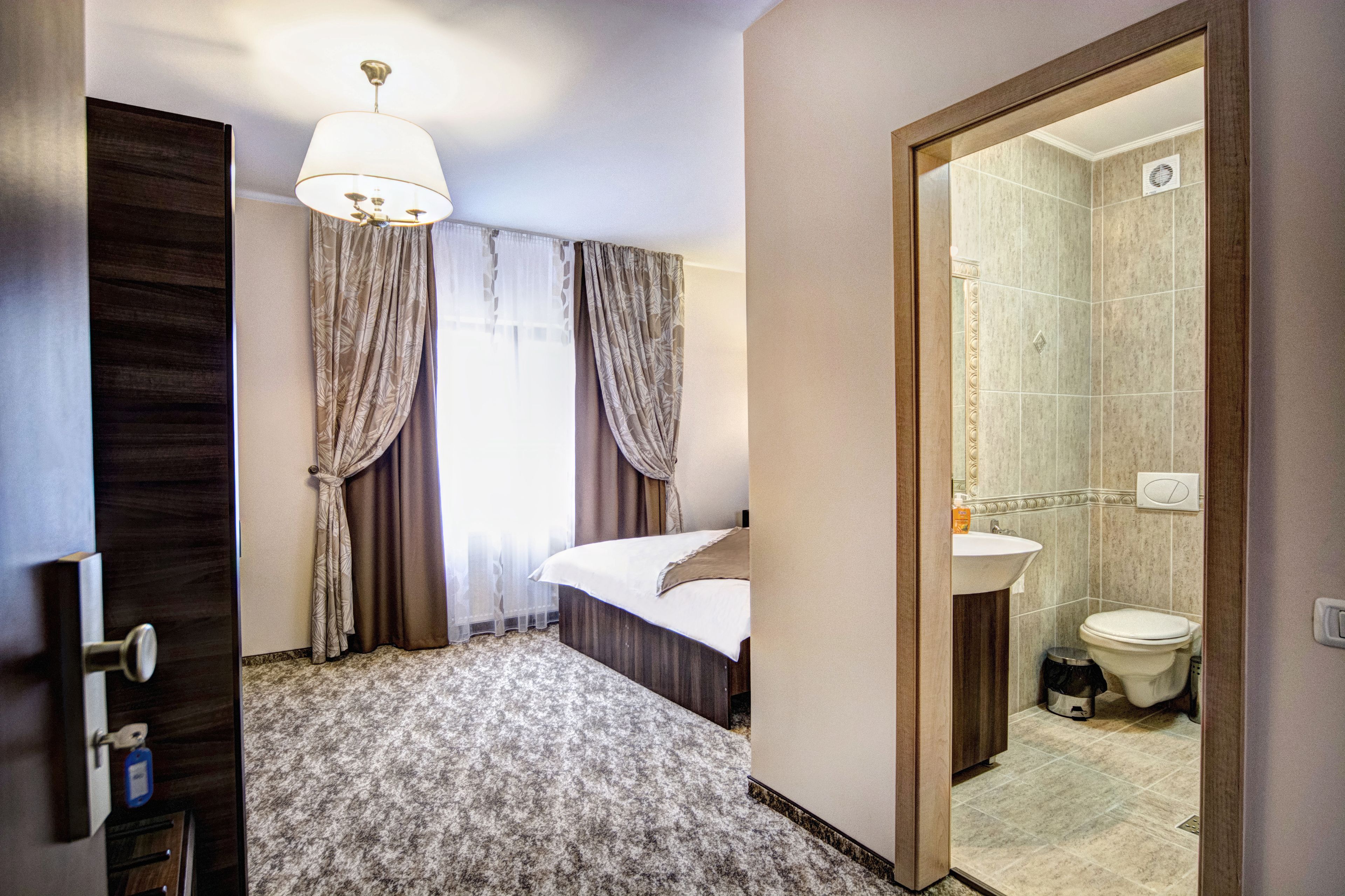 Una habitación de hotel con una cama, un baño con lavamanos e inodoro, y una puerta que da a otra habitación.