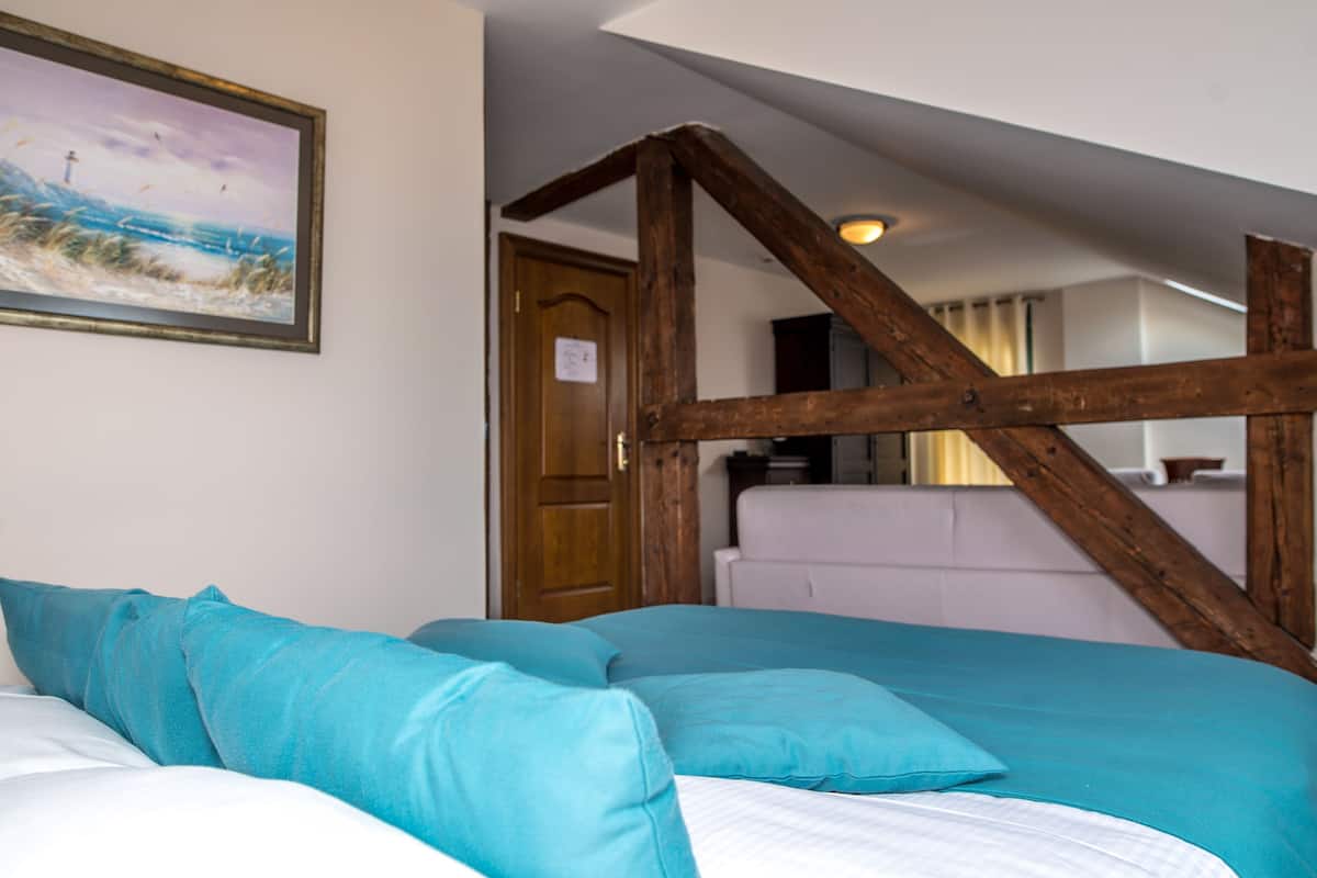 Un dormitorio con viga de madera en el techo, una cama con ropa de cama color turquesa y un cuadro con una playa.