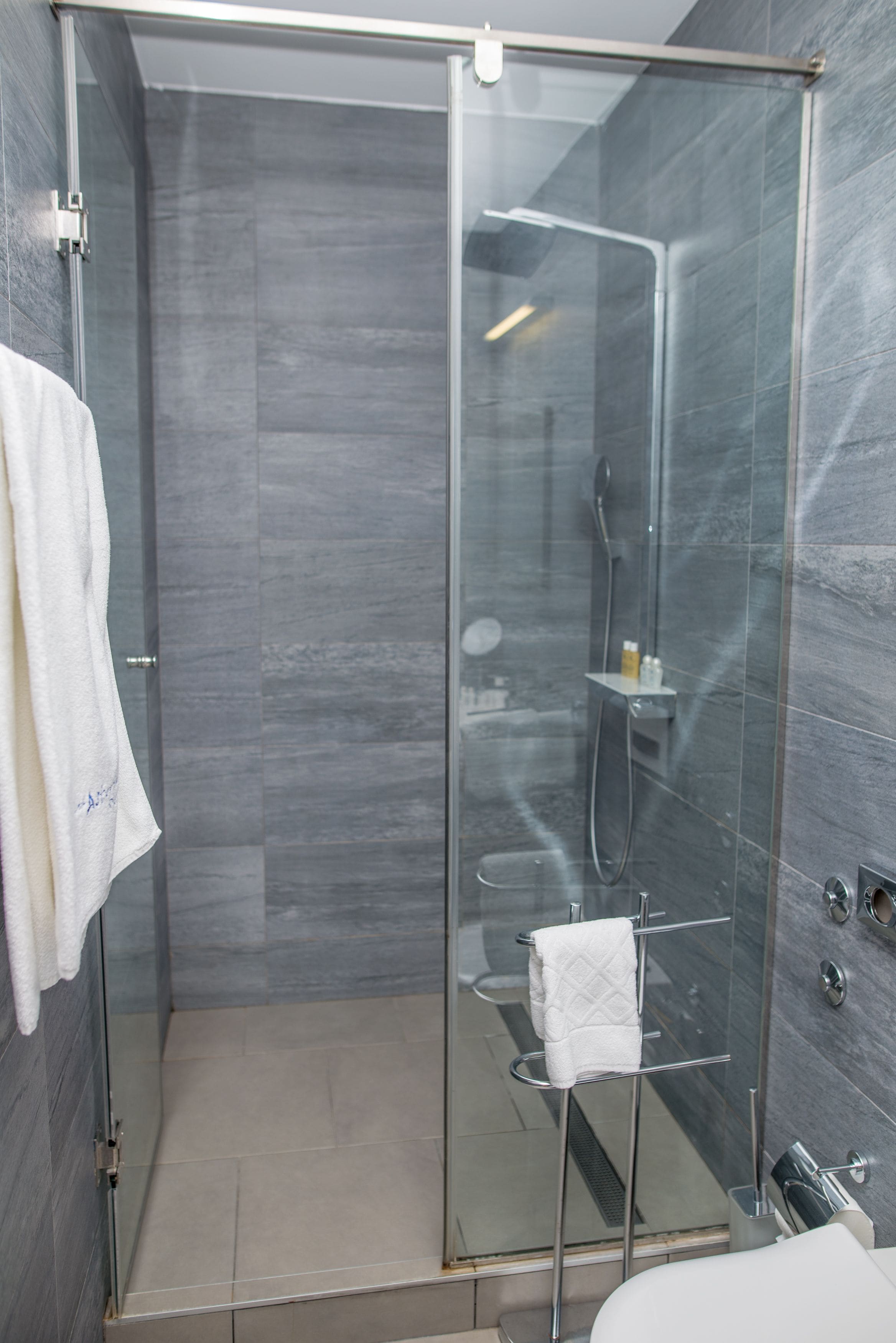 A modern shower area with a glass door, a towel rack, and a small shelf with toiletries.