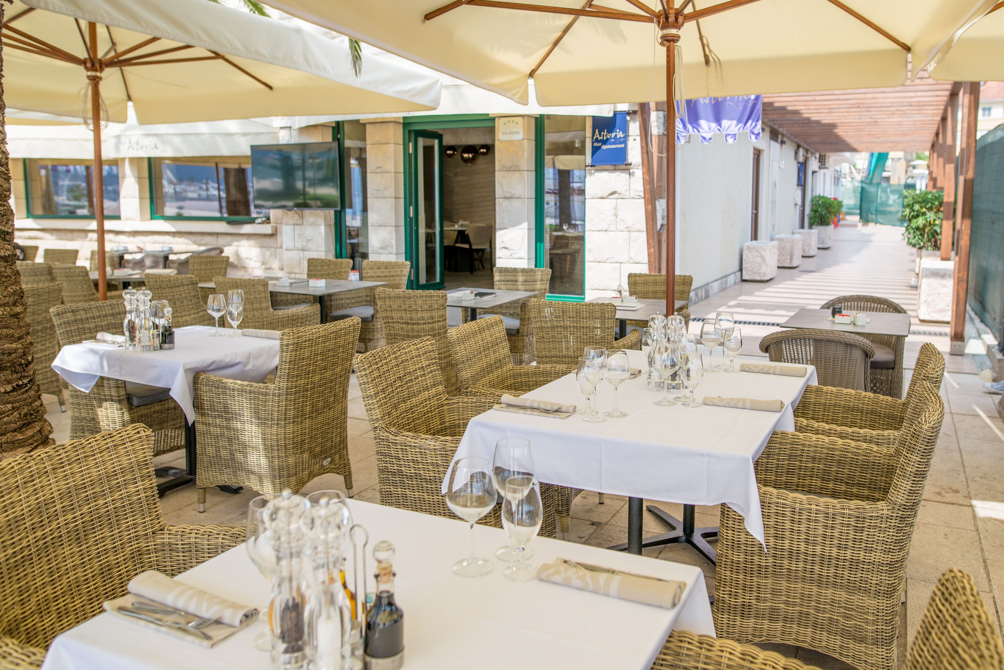 Zona pranzo all'aperto con mobili in vimini e tovaglie bianche.