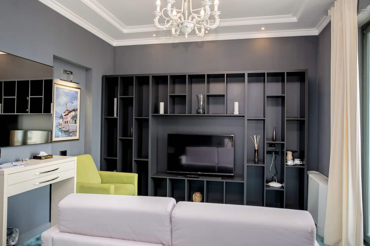 Un salón moderno con televisor de pantalla plana, estanterías empotradas, un escritorio blanco y una silla verde.