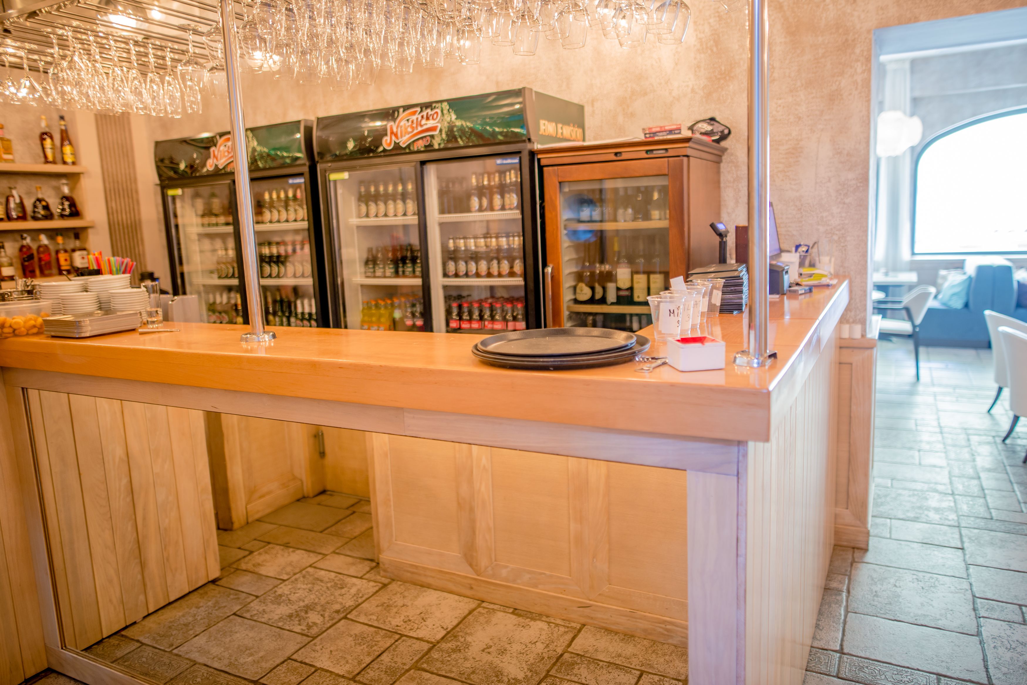 Zona de bar con mostrador de madera, estantes con botellas y un refrigerador.