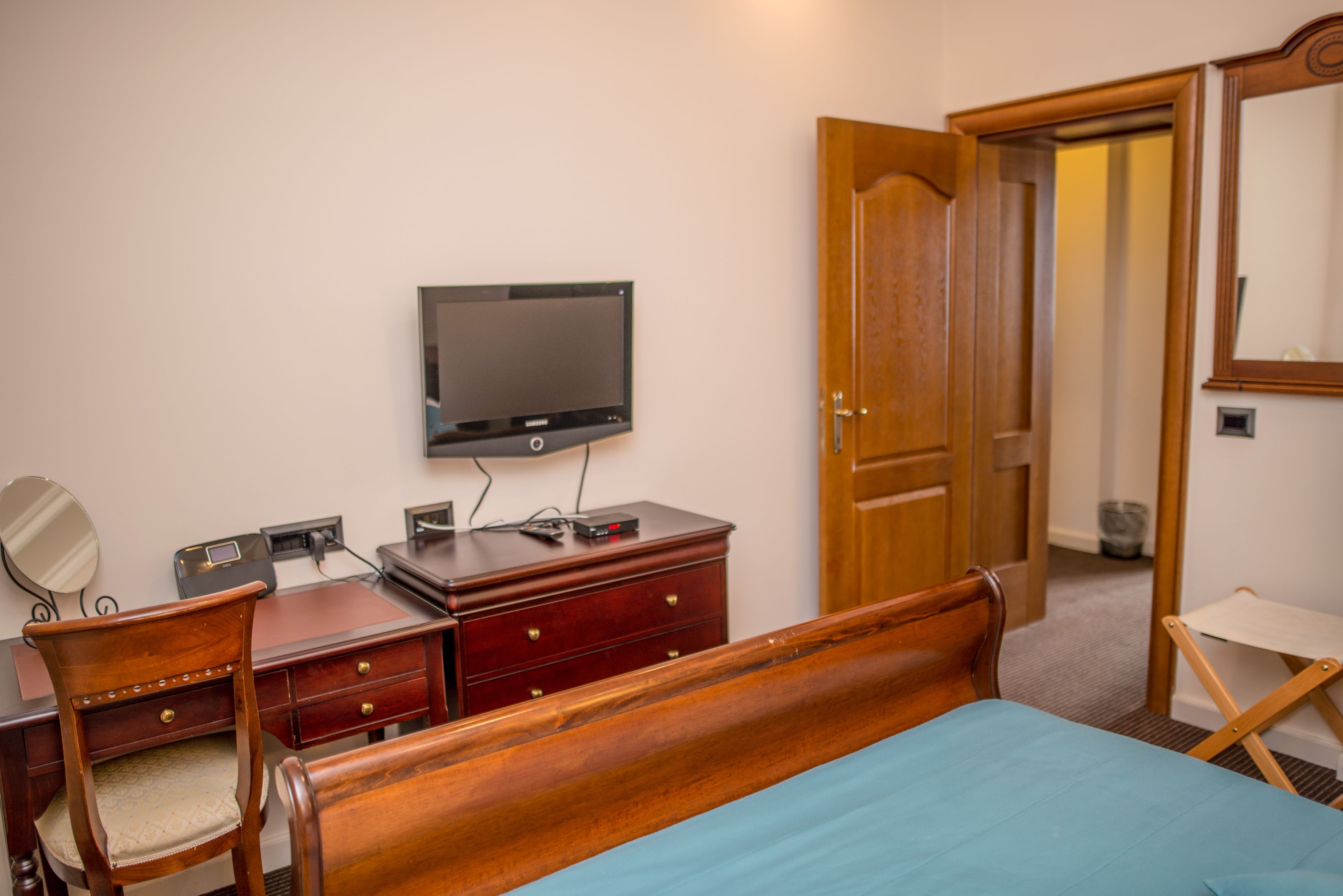 Un dormitorio con una cama de madera, un escritorio con televisor, un aparador y un espejo.