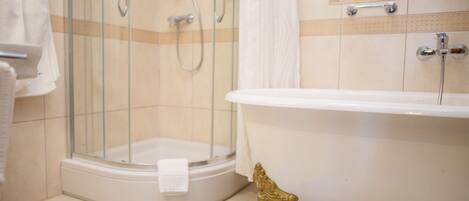 A bathroom with a glass-enclosed shower, a white bathtub, and a gold decorative element.