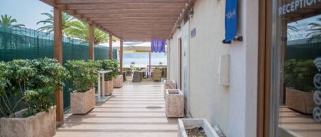 A covered outdoor area with a reception desk, potted plants, and a view of the sea.