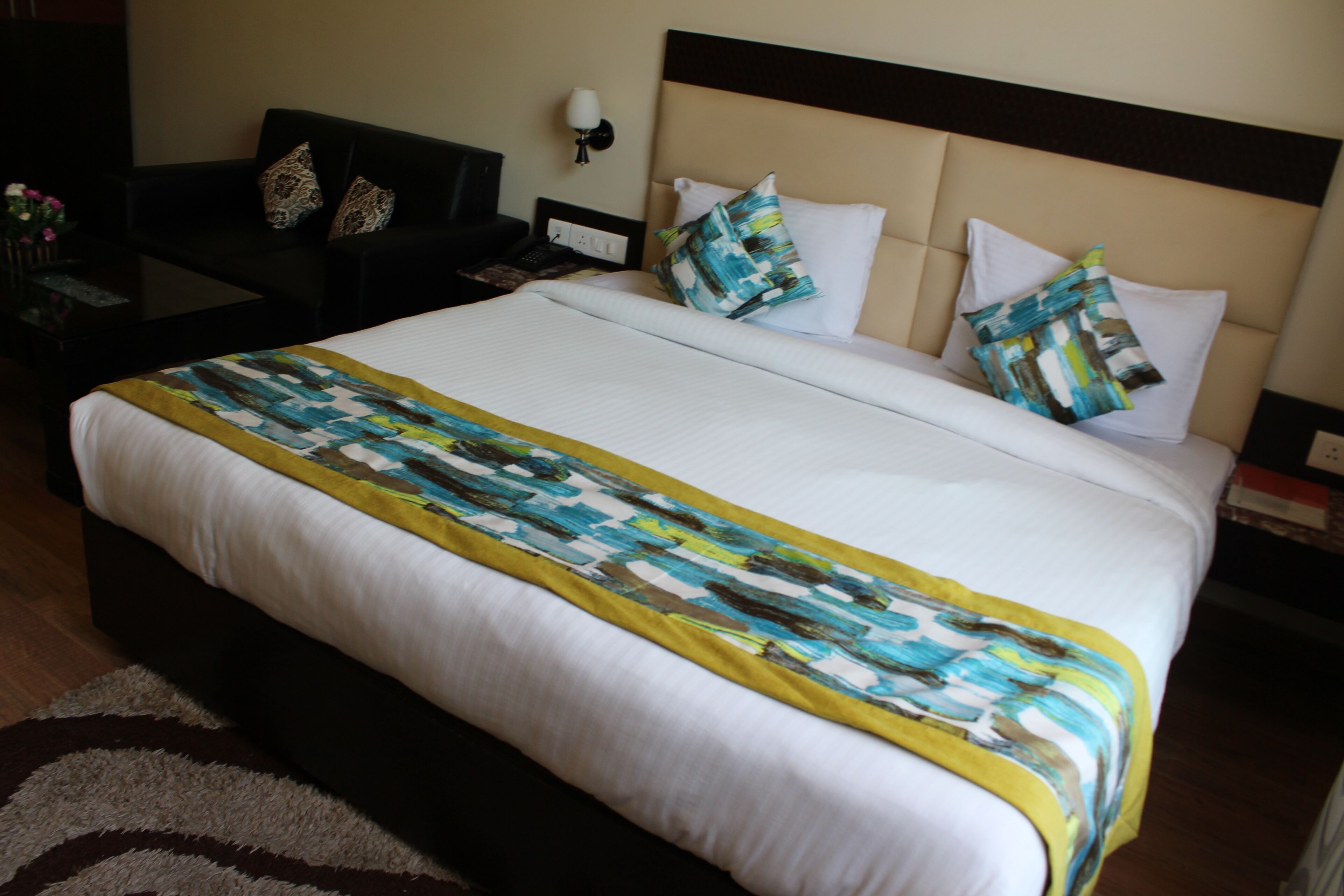 A hotel room with a large bed, a nightstand, a lamp, and a desk with a telephone.