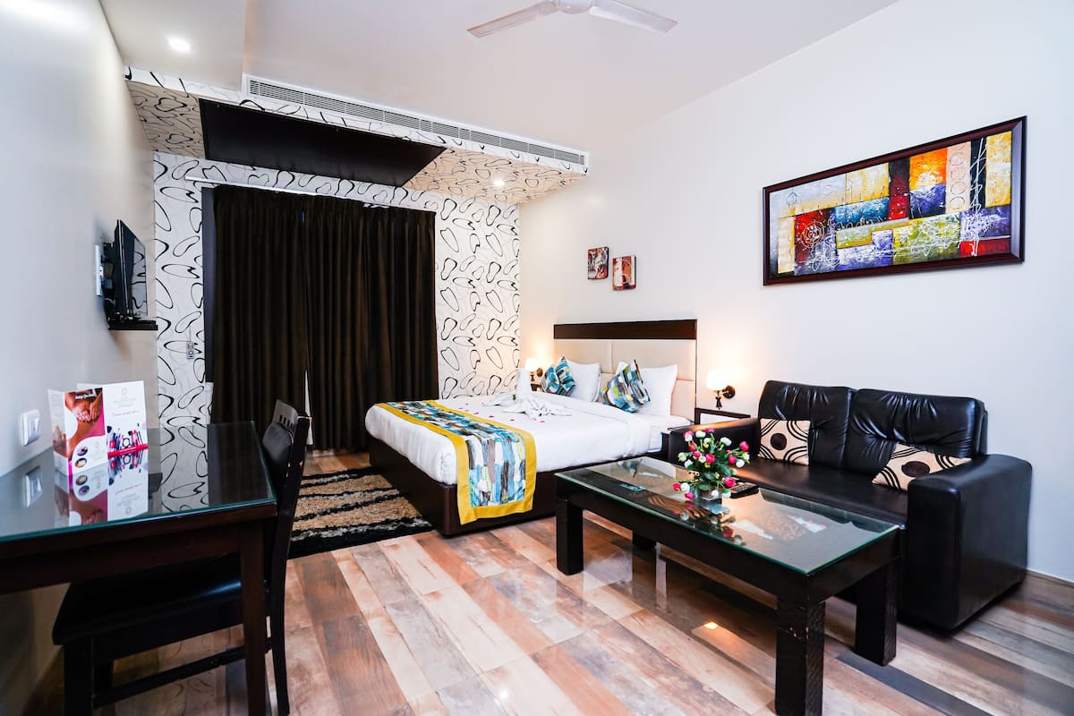 A modern hotel room with a bed, a sofa, a coffee table, and a TV.