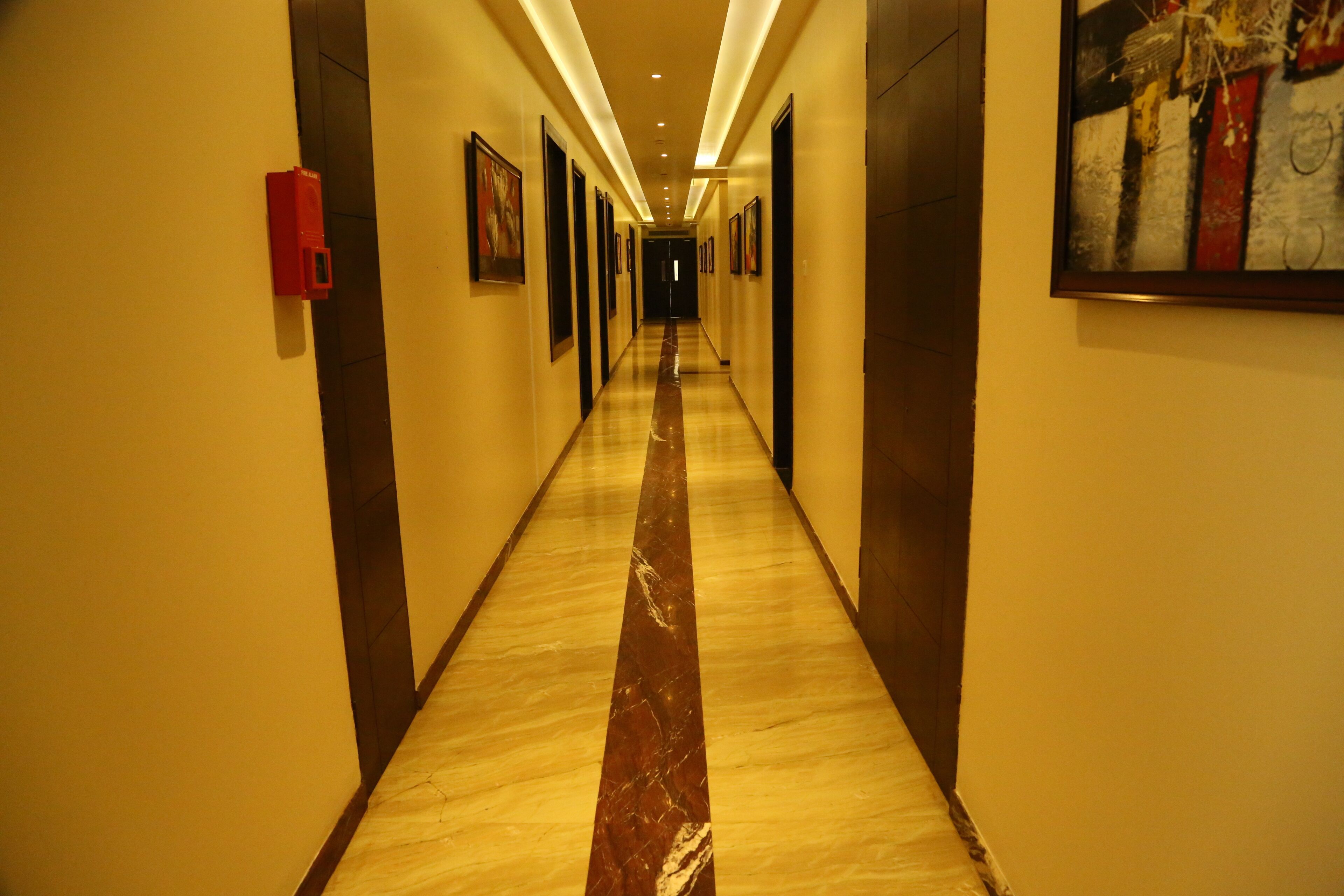 A long, narrow hallway with a marble floor, doors on both sides, and framed artwork on the walls.