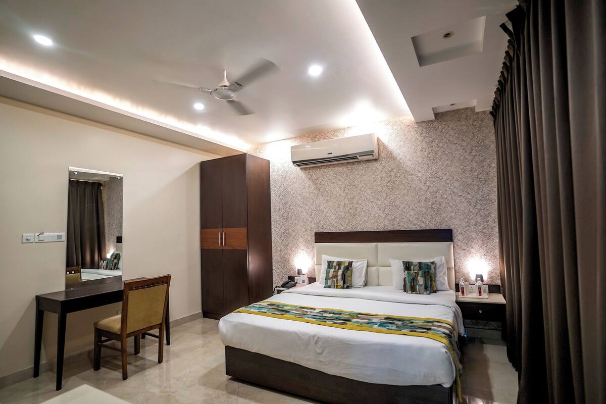 A hotel room with a bed, desk, chair, and an air conditioning unit.