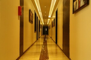 Un largo pasillo de hotel, estrecho, con suelo de mármol pulido, obras de arte enmarcadas en las paredes e iluminación empotrada.