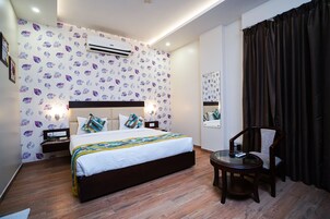 Una habitación de hotel con cama, mesitas de noche, una silla, un escritorio, un aire acondicionado y un espejo en la pared.