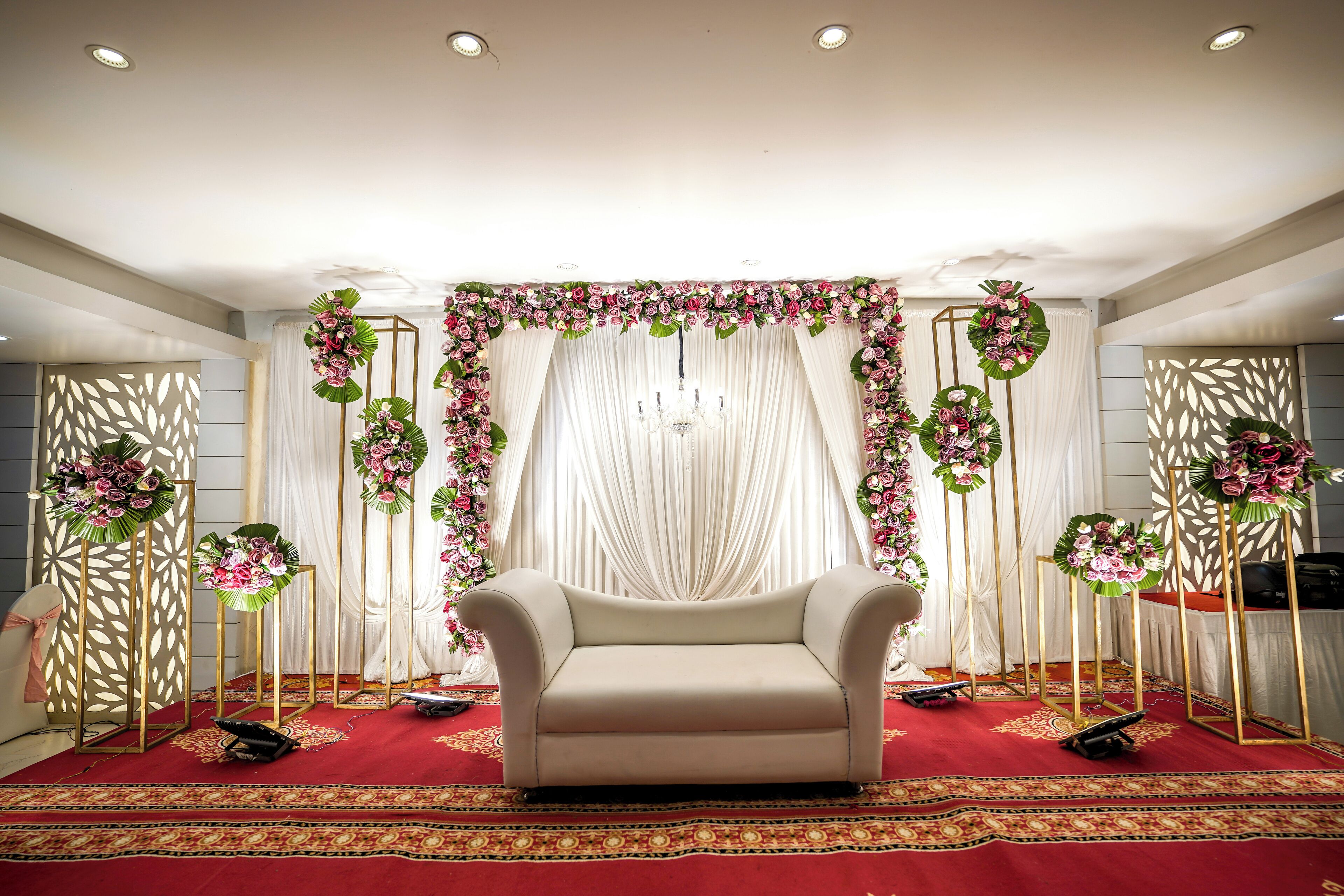 A stage with a sofa, draped curtains, and floral arrangements.