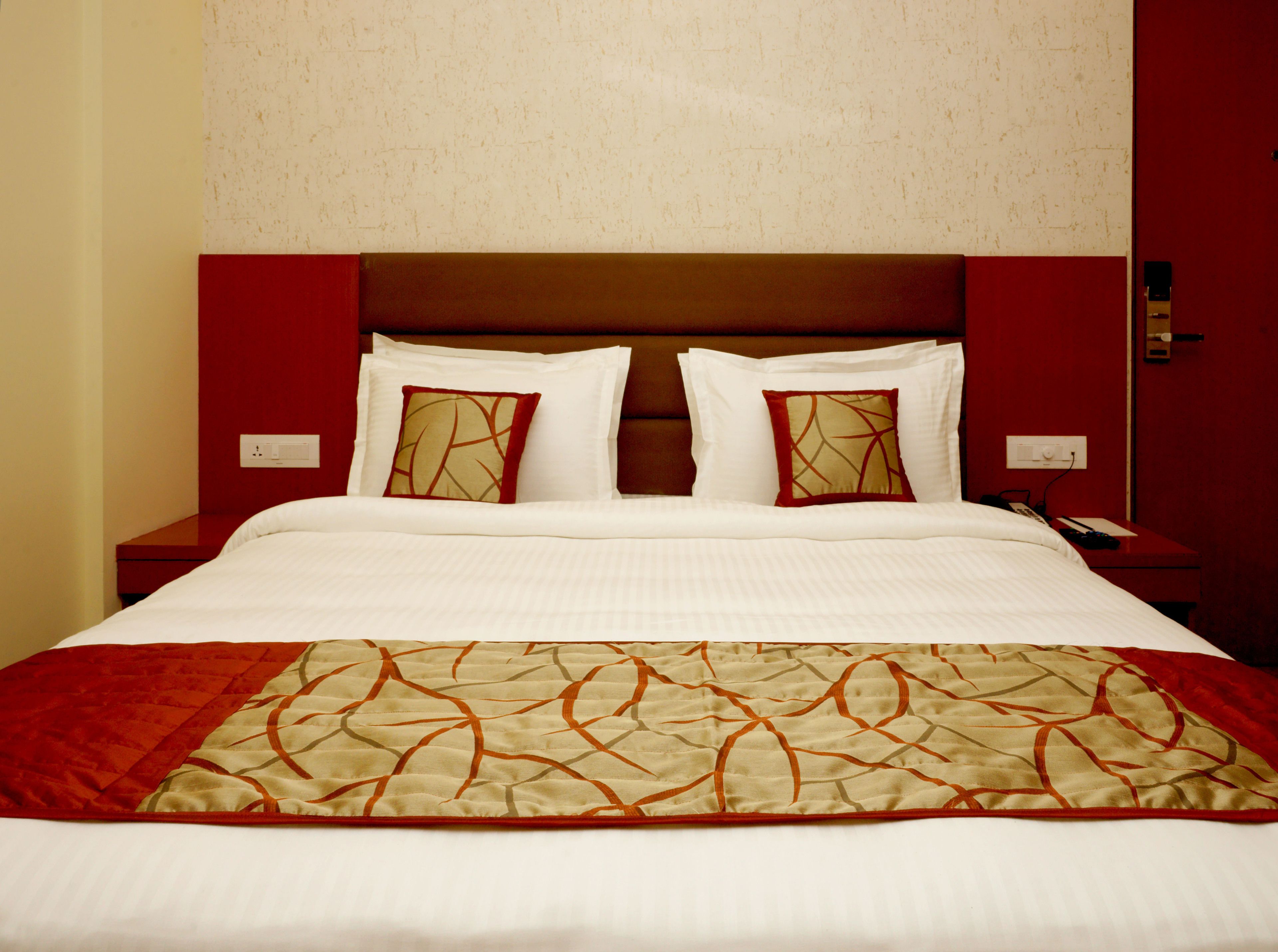 Habitación de hotel con una cama bien hecha, una pared de acento roja y un cabecero de madera.