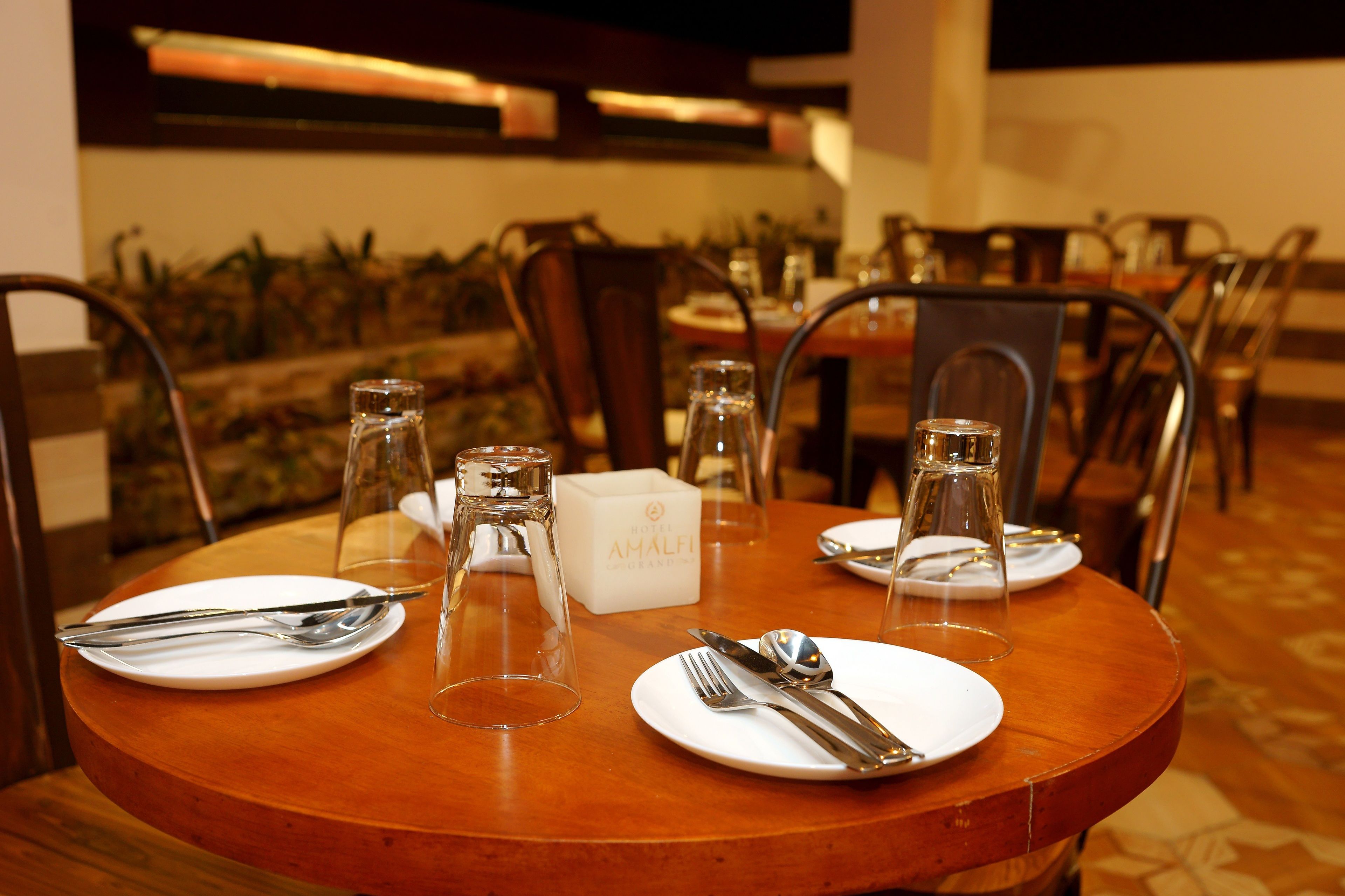Une table à manger dressée avec des assiettes, des couverts et des verres, et une boîte portant l’inscription « AMALFI » placée au centre.