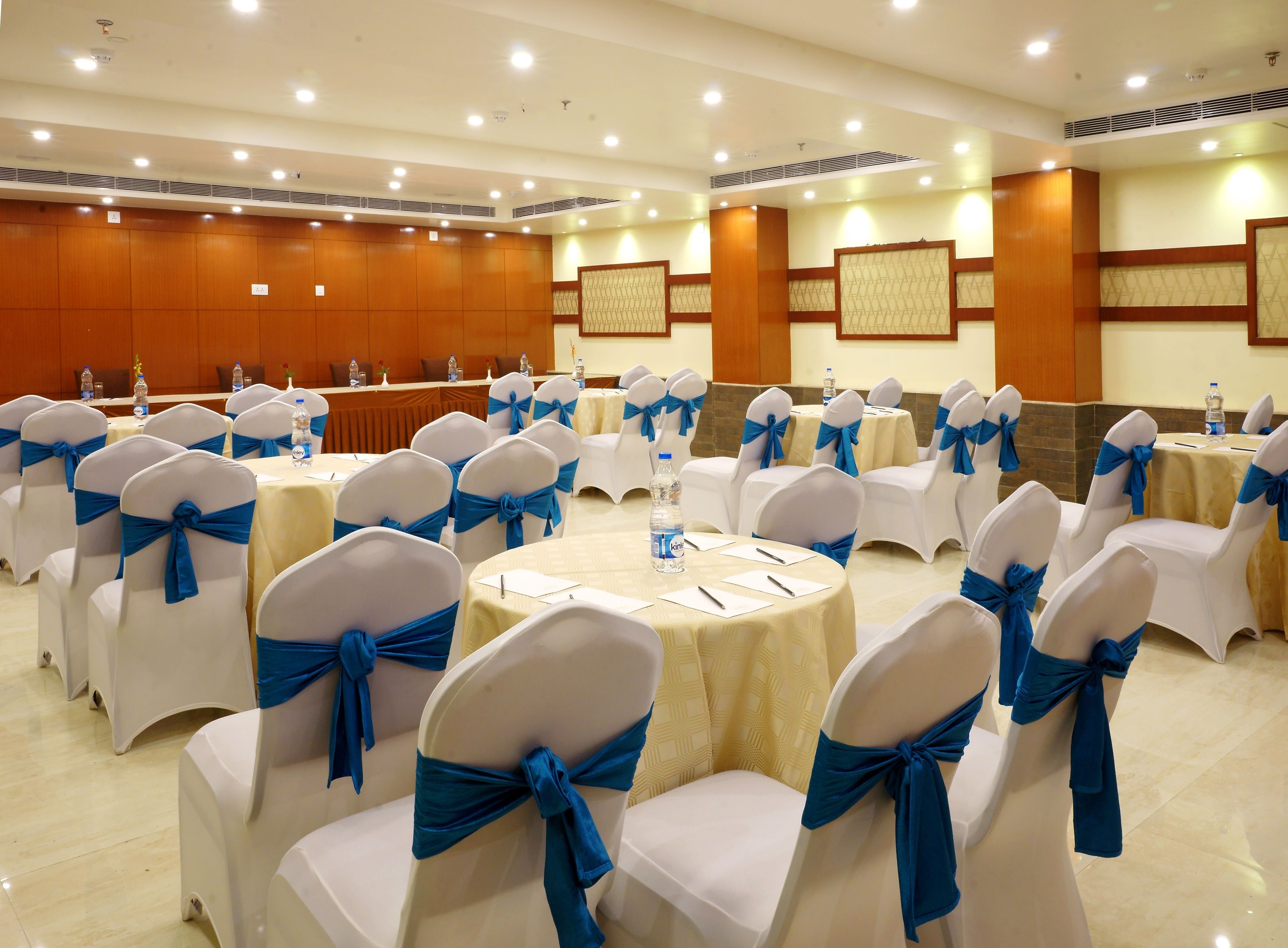 A conference room with round tables, white chairs with blue sashes, and a long table with water bottles.