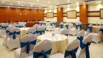 A conference room with round tables, white chairs with blue sashes, and a long table with water bottles.