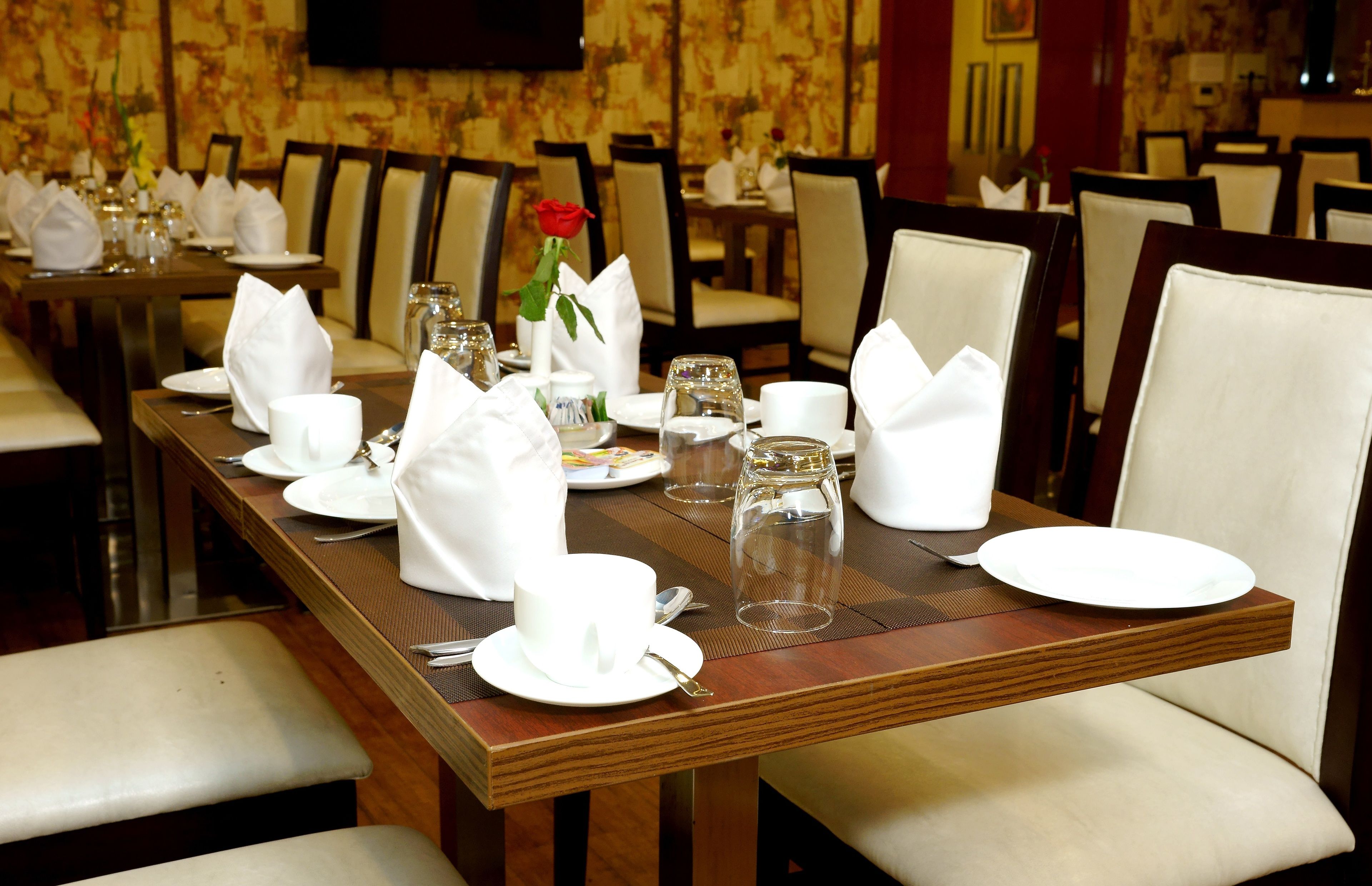 A dining table set with white napkins, plates, and glassware, with a rose centerpiece.