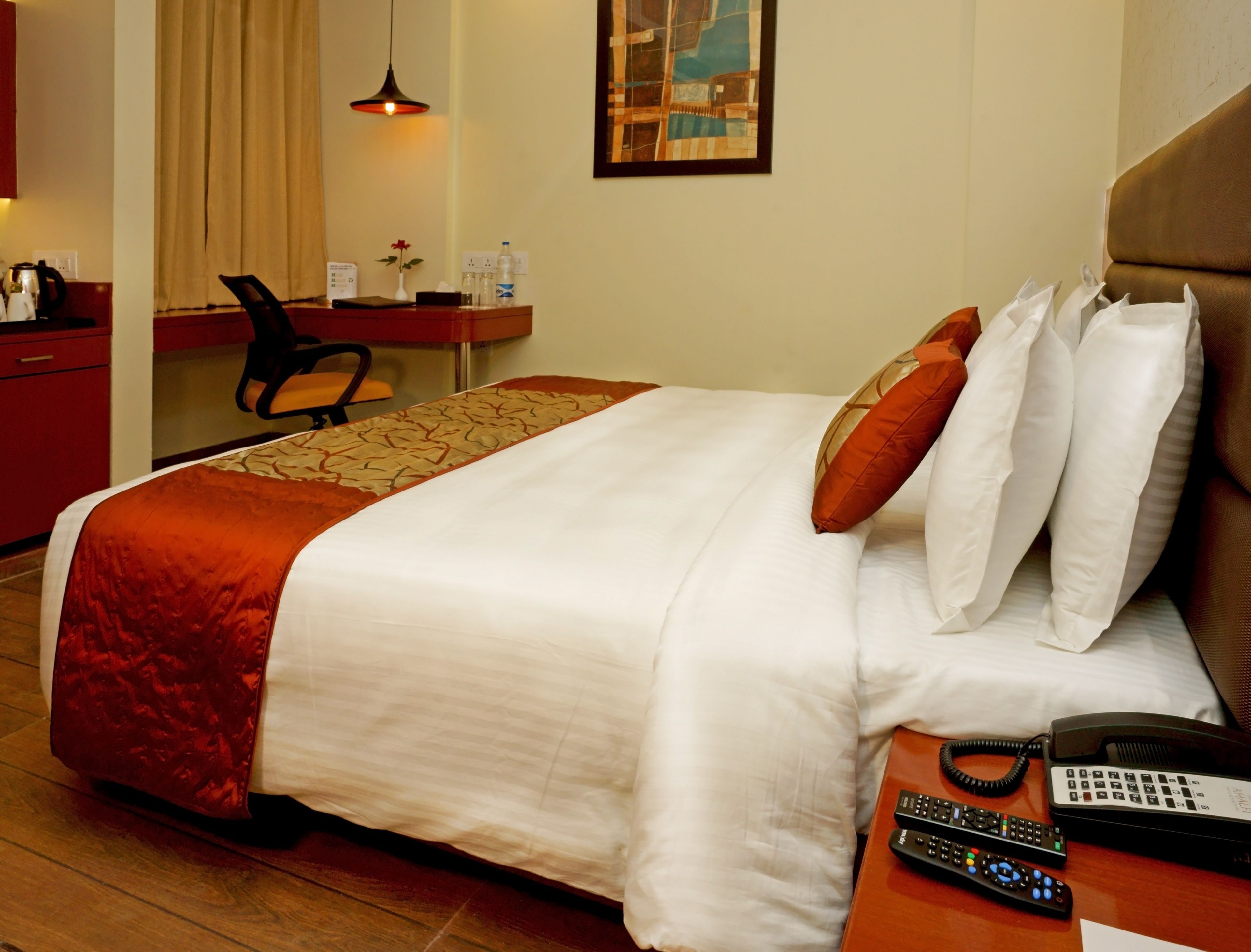 A hotel room with a bed, a desk, a chair, a telephone, and a remote control.