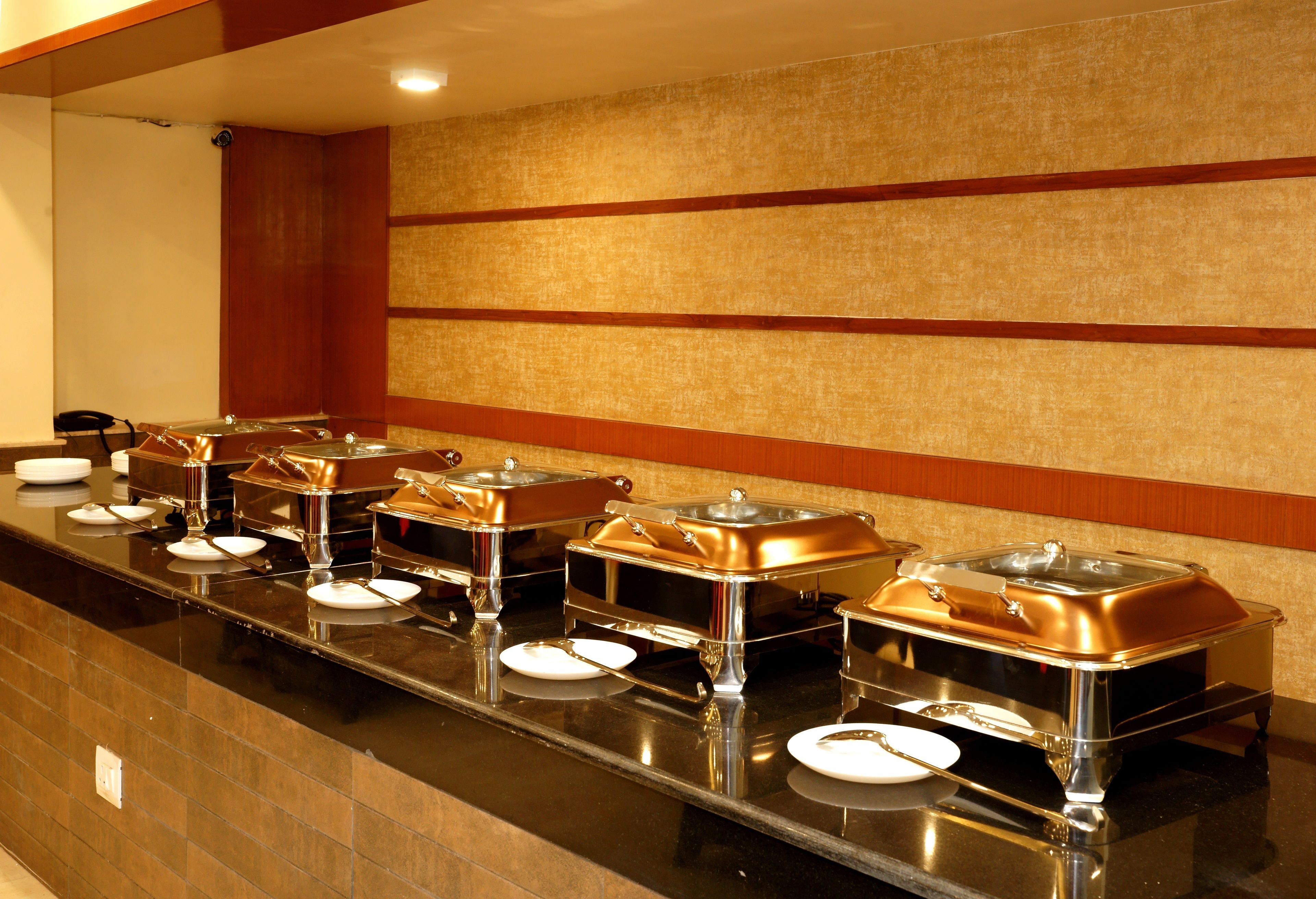 Un buffet con múltiples estaciones de servicio, cada una con un recipiente para alimentos cubierto y un plato.