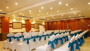 Un salón de conferencias con filas de sillas blancas con cintas azules, un papel tapiz estampado y una puerta de madera.