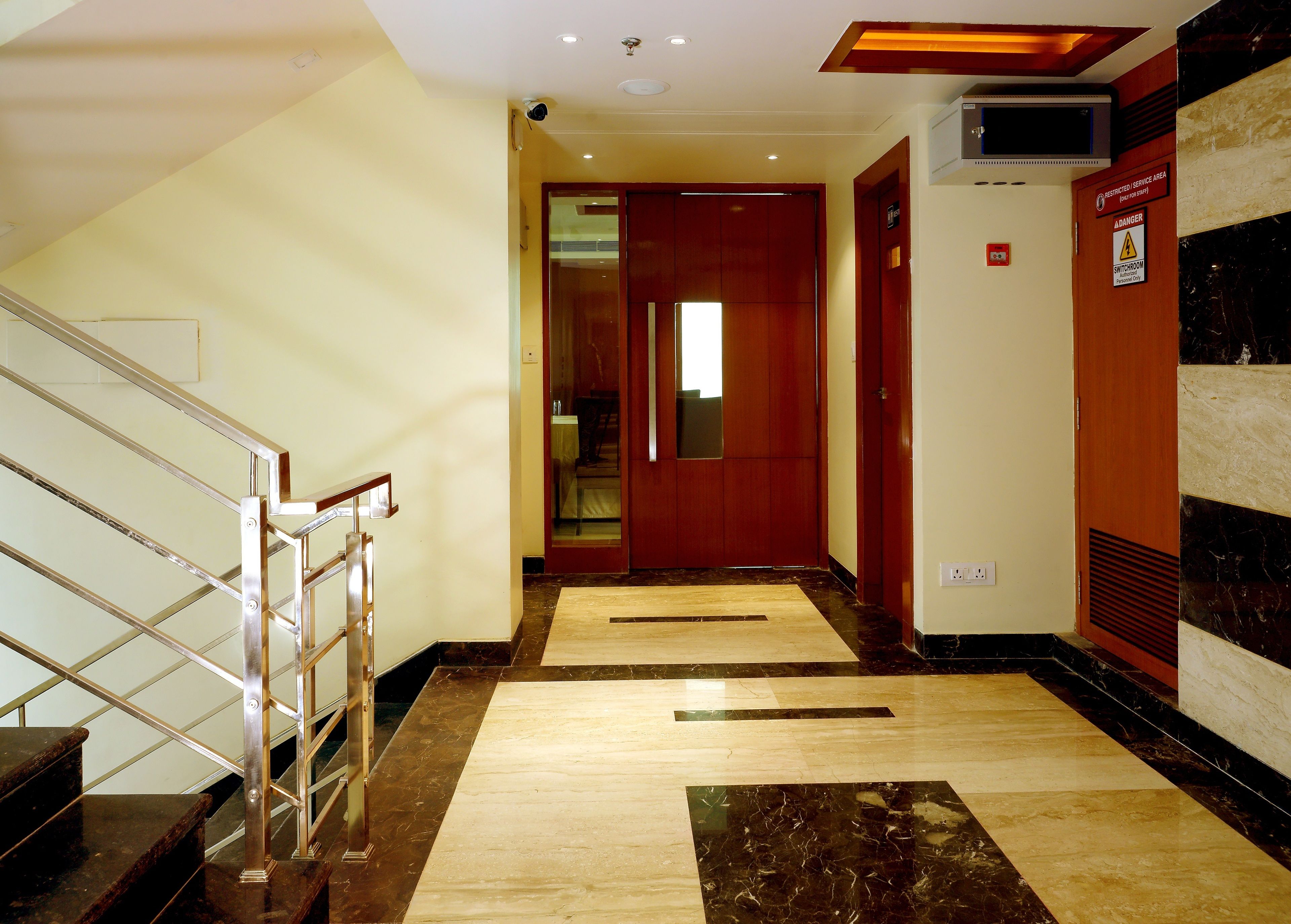 A hotel corridor with a marble floor, a staircase with metal railings, and a wooden door at the end.
