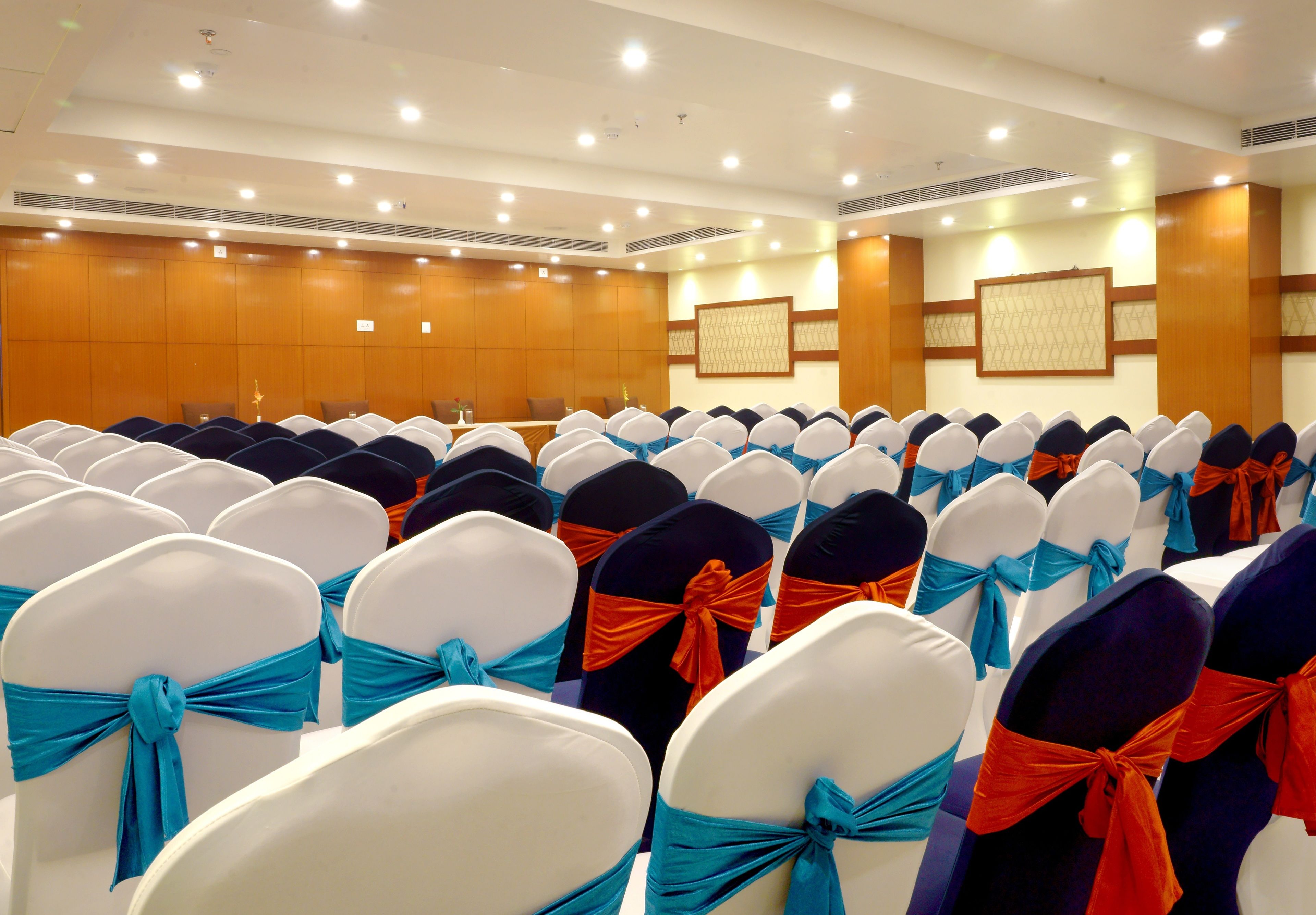 A conference room with rows of chairs, some with blue and orange sashes, and wooden paneling on the walls.