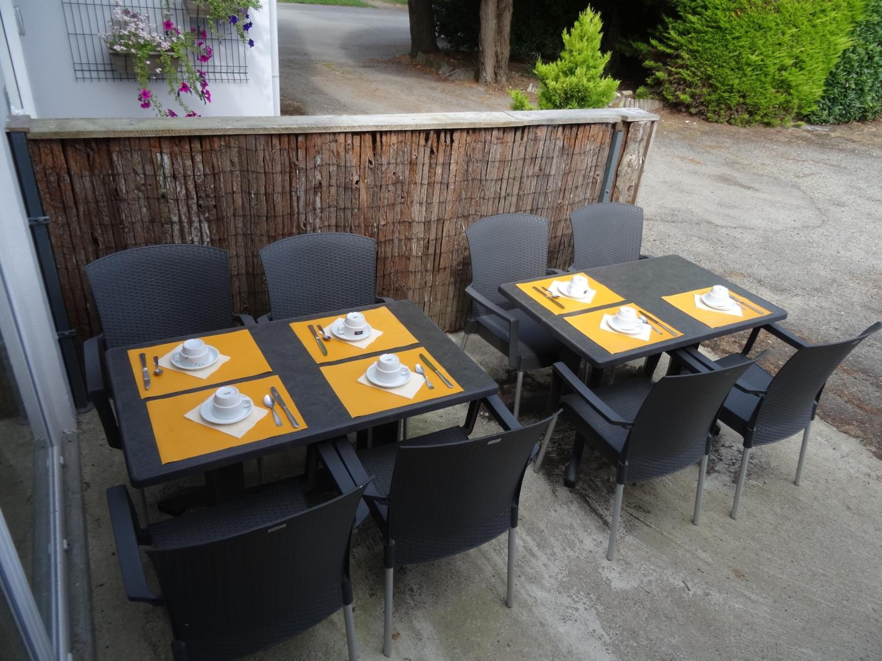 Un espace extérieur aménagé pour les repas, avec des tables et des chaises, une clôture en bois et une vue sur le jardin.