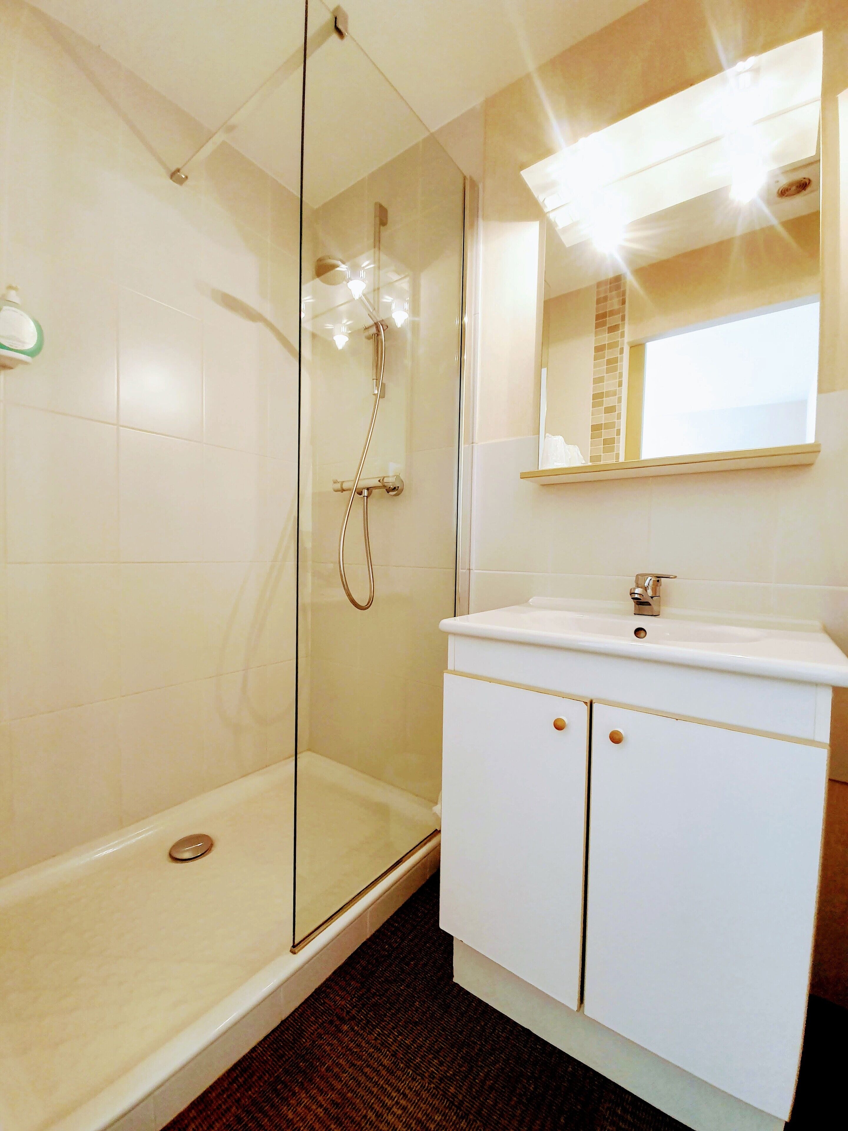 A modern bathroom with a glass-enclosed shower, a white vanity with a mirror, and a tiled floor.