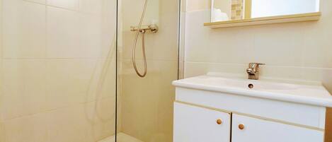 A modern bathroom with a glass-enclosed shower, a white vanity with a mirror, and a tiled floor.