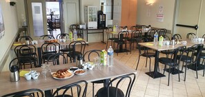 Comedor con varias mesas y sillas, equipado con diferentes comodidades como botellas de agua, vasos y una máquina de café.