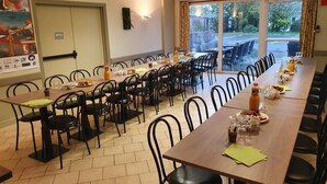 A hotel dining area with multiple tables and chairs, a projector screen, and a view of the outdoors through large windows. - Le Toul' Broch (Baden)