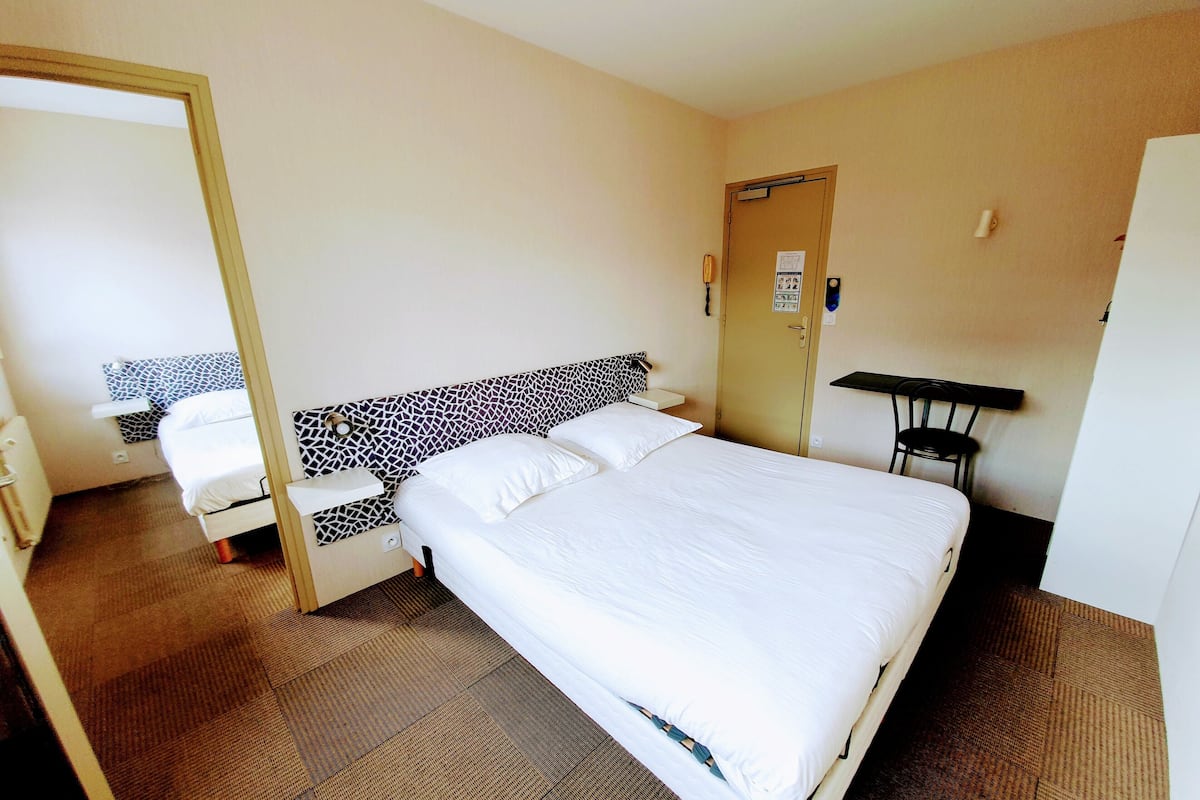 A hotel room with a large bed, a bedside table, a chair, and a desk.