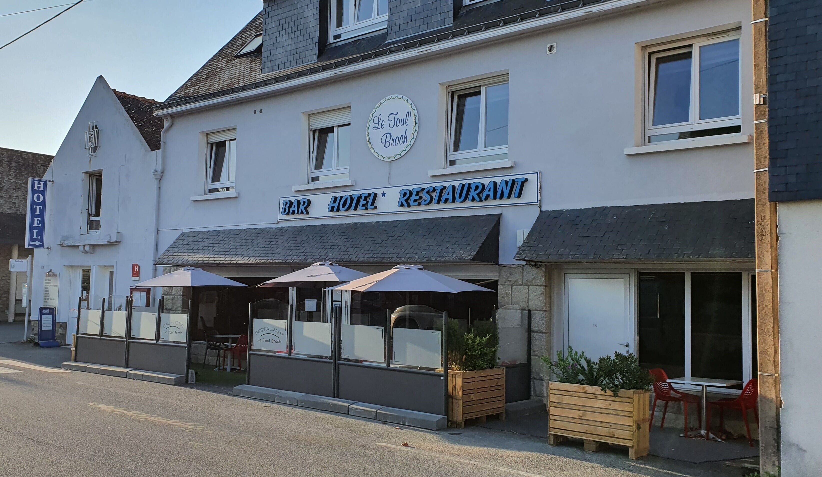 Un hôtel doté d’un bar et d’un restaurant, avec une terrasse offrant des places assises à l’extérieur, des parasols et des jardinières en bois.