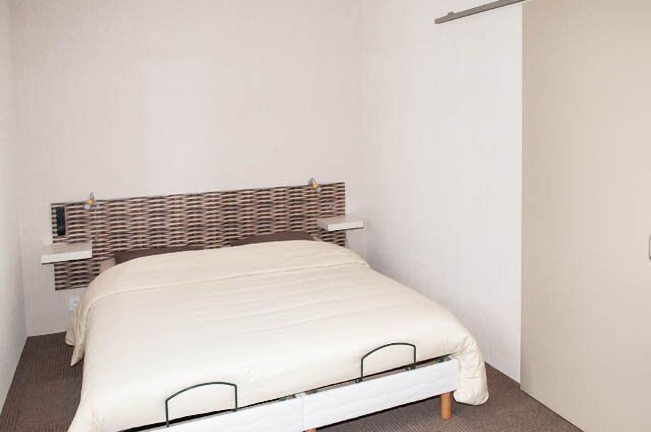 Un llit individual amb un capçal trenat, una taula de nit i una paret senzilla.
