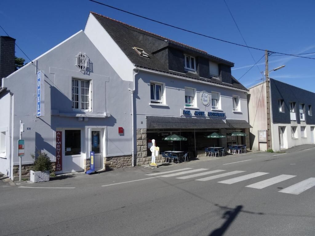 Un bâtiment à deux étages, avec une enseigne indiquant la présence d’un hôtel et d’un restaurant. On y trouve des tables et des chaises à l’extérieur, devant le bâtiment.