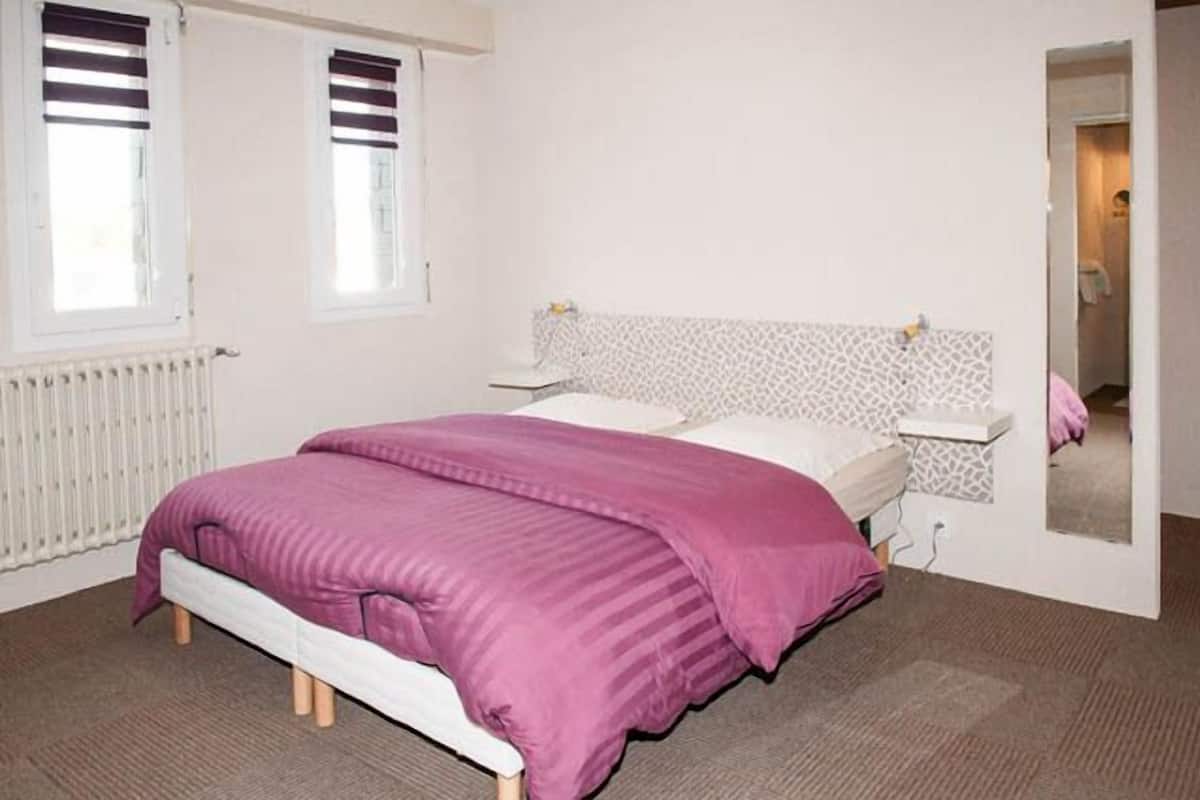 A bedroom with a bed, a bedside table, a radiator, and a window with blinds.