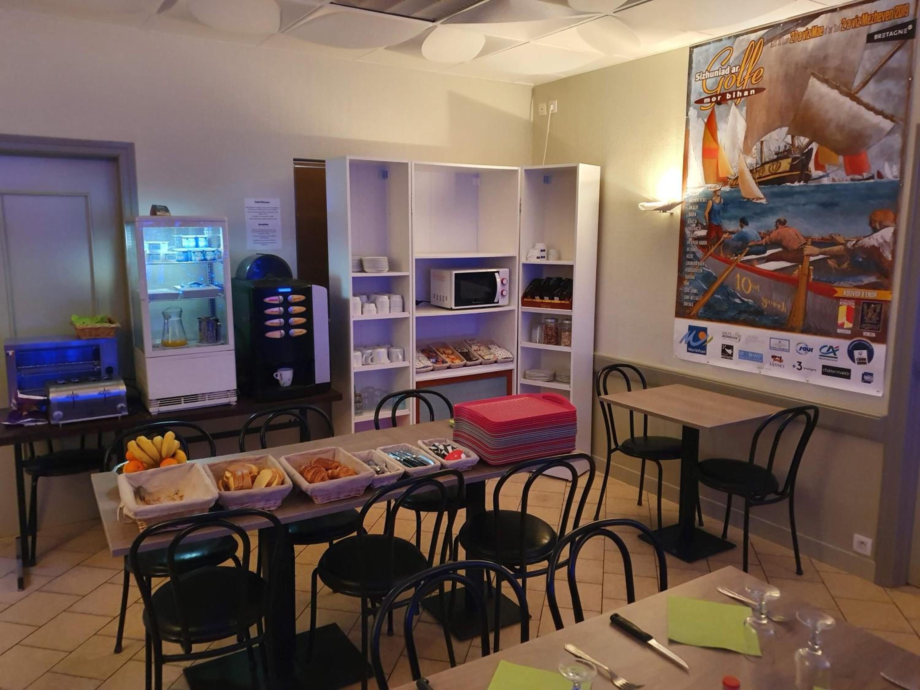 Un espace repas comprenant une table de buffet, des chaises, un réfrigérateur et une affiche accrochée au mur.