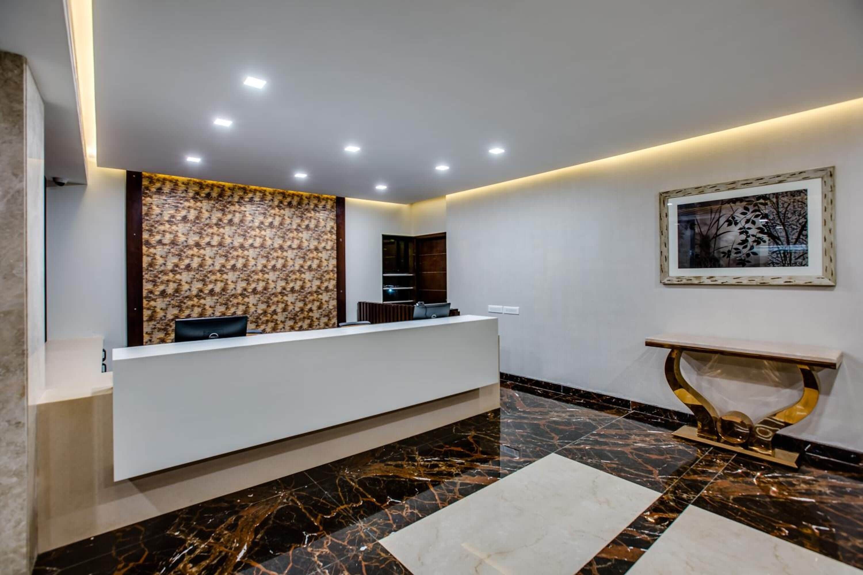 A reception area with a marble floor, a reception desk, a patterned wall, and a framed artwork on the wall.