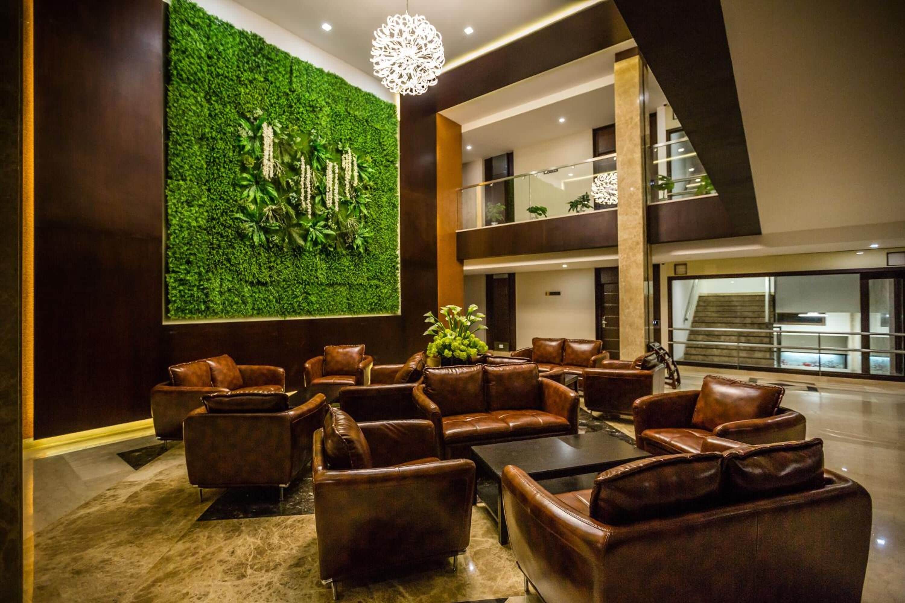 A modern lobby with leather sofas, a green wall with plants, and a staircase.
