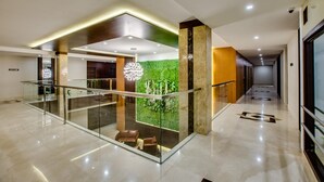 Um hall de hotel moderno com guarda-corpo de vidro, uma parede verde com plantas e uma área de estar.