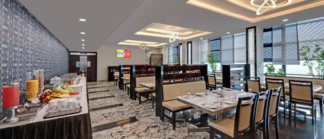 Un ristorante moderno con pavimento in marmo, sedute in legno e un'area buffet con frutta e bevande.