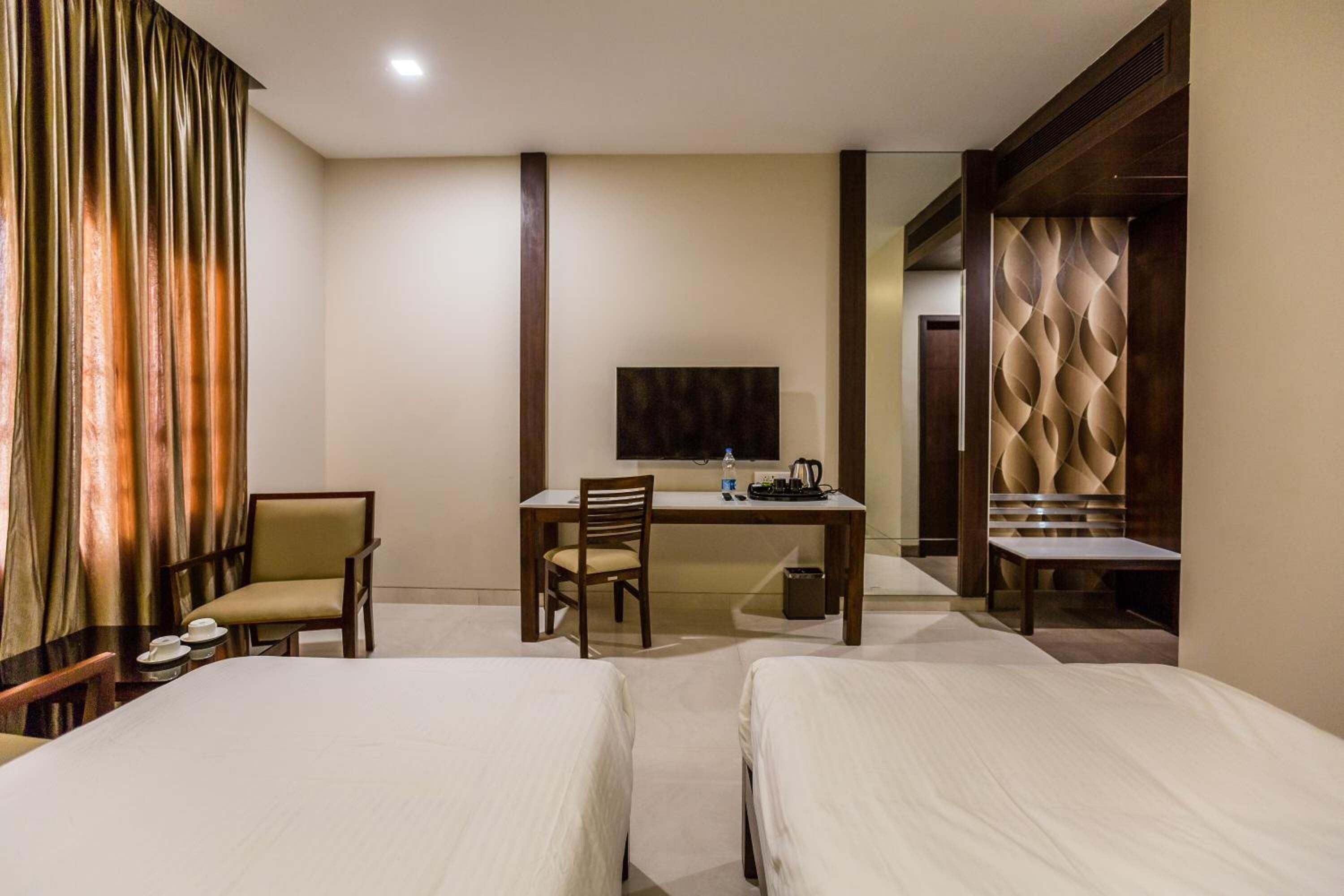 Quarto de hotel com duas camas, uma escrivaninha com cadeira, televisão e espelho.