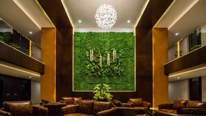 Um hall com sofás de couro, parede verde com plantas e um lustre decorativo.