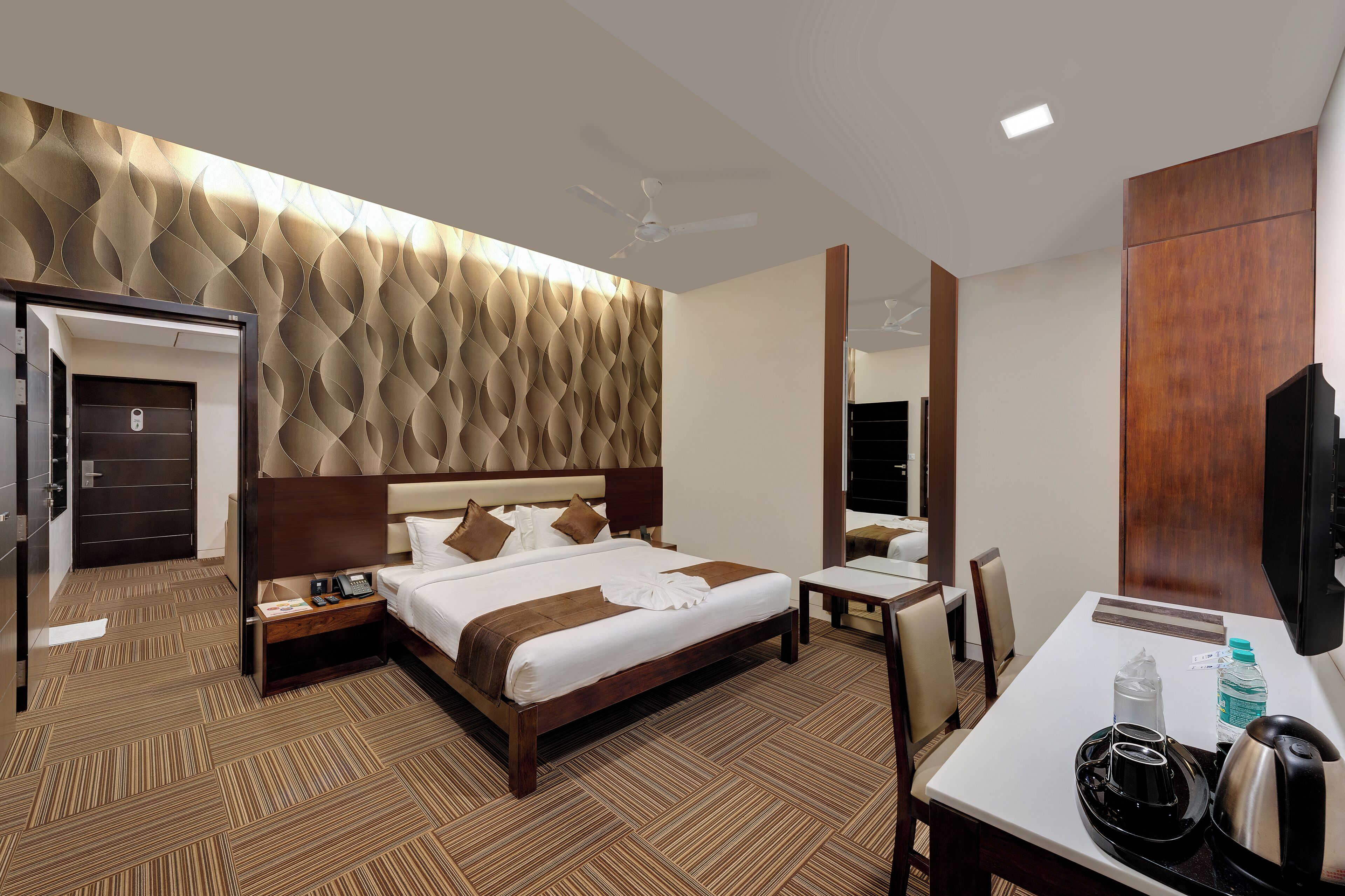 A hotel room with a large bed, a desk with a chair, a flat-screen TV, a coffee maker, and a water bottle.