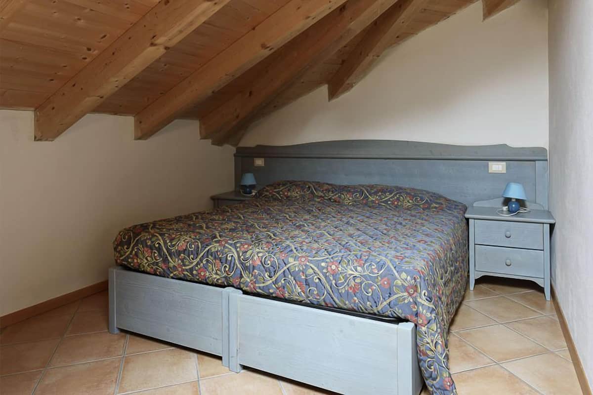 Ein Schlafzimmer mit Holzboden, einem Bett mit gemustertem Überwurf, zwei Nachttischen mit Lampen und einer kleinen Schublade unter dem Bett.