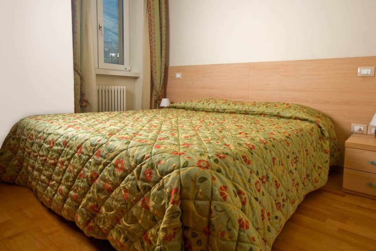 Ein Schlafzimmer mit einem hölzernen Kopfteil, einer blumigen Bettdecke, einem Nachttisch und einem Fenster mit Vorhängen.