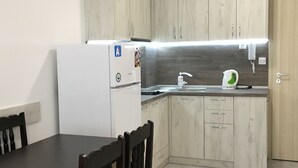 A compact kitchen with wooden cabinets, a white refrigerator, a sink, and a dining area with chairs. - VIP Zone Apartments (Sunny Beach)