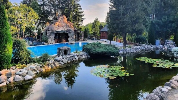 Un área de piscina tranquila al aire libre, con una formación rocosa natural, rodeada de vegetación exuberante y árboles altos.