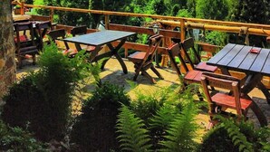 Un espacio al aire libre con mesas y sillas, rodeado de exuberante vegetación y un paisaje montañoso al fondo.