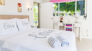 A neatly made bed with rolled towels, a desk with a lamp, and a window with a view of greenery. - Casalina Garden Apartment Aruba (Noord)